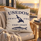 Cozy Coast Kissenhülle USEDOM 50 x 50 cm in Natur mit dunkelblauer Inselsilhouette, Koordinaten und Fischmotiv auf einem Rattansessel auf einer Terrasse mit Blick auf die Ostsee bei Sonnenuntergang